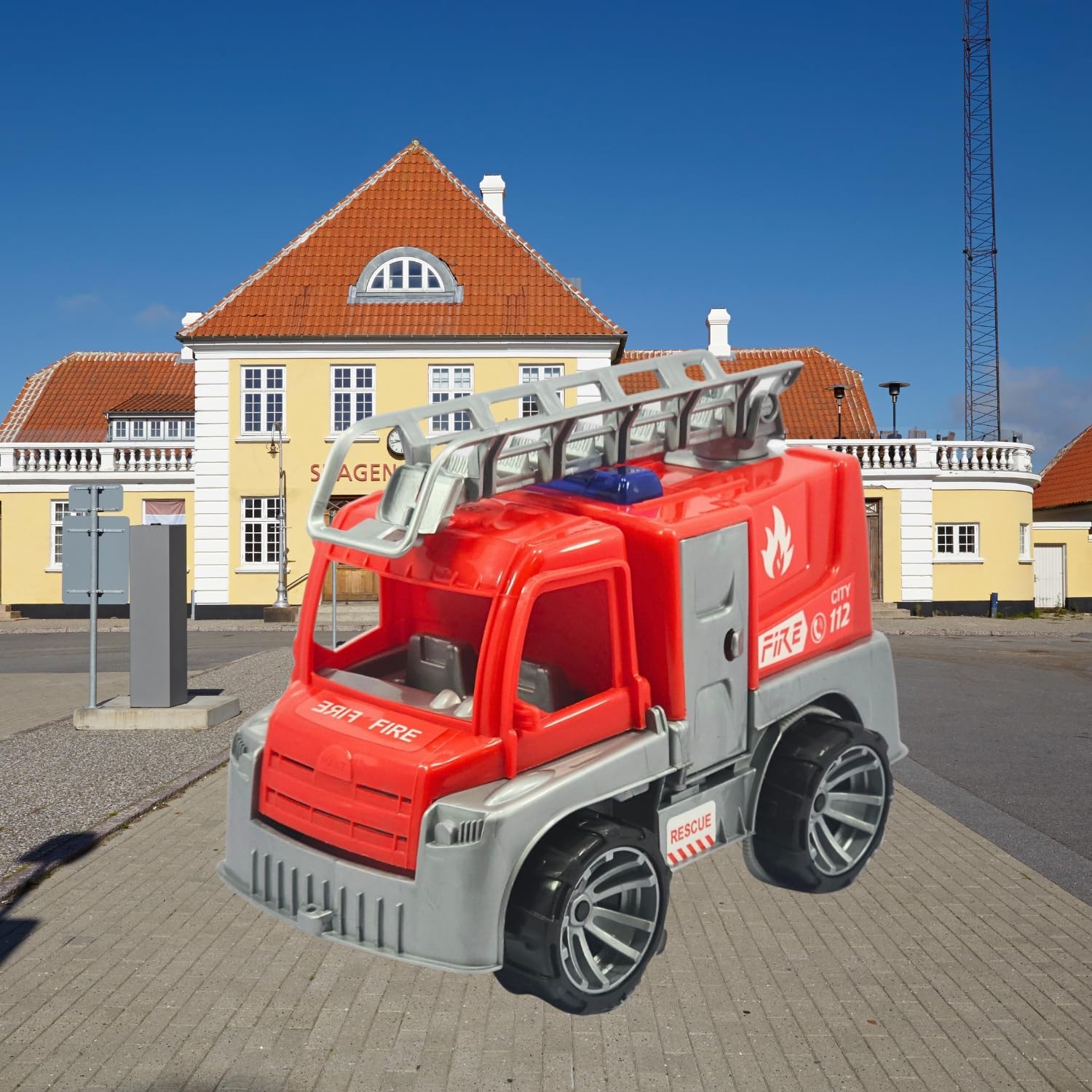 Red toy fire truck on a street with a building in the background
