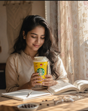 Woman holding a Starbucks coffee cup with a book open on a table.
