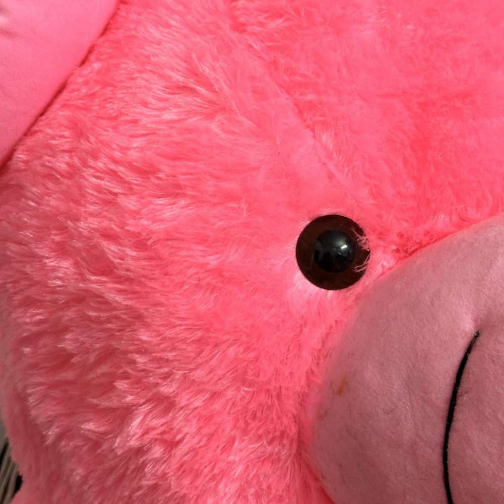 Close-up of a pink plush toy with a black button on its chest.