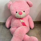 Large pink teddy bear sitting on a concrete floor against a white wall.